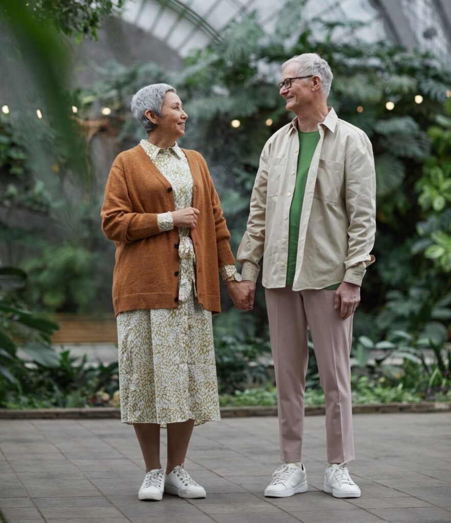 Smiling older couple holding hands while walking together in a leafy glasshouse